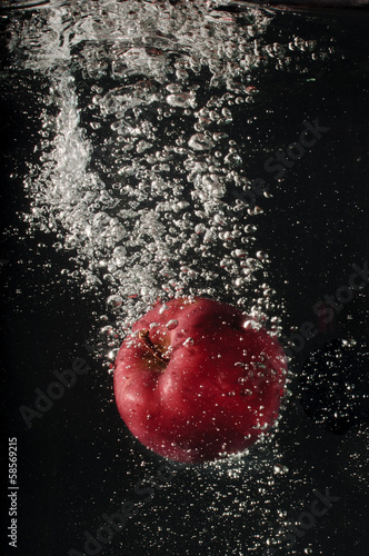 Red apple falling into water on black background