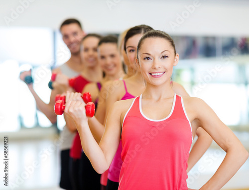 group of smiling people with dumbbells in the gym