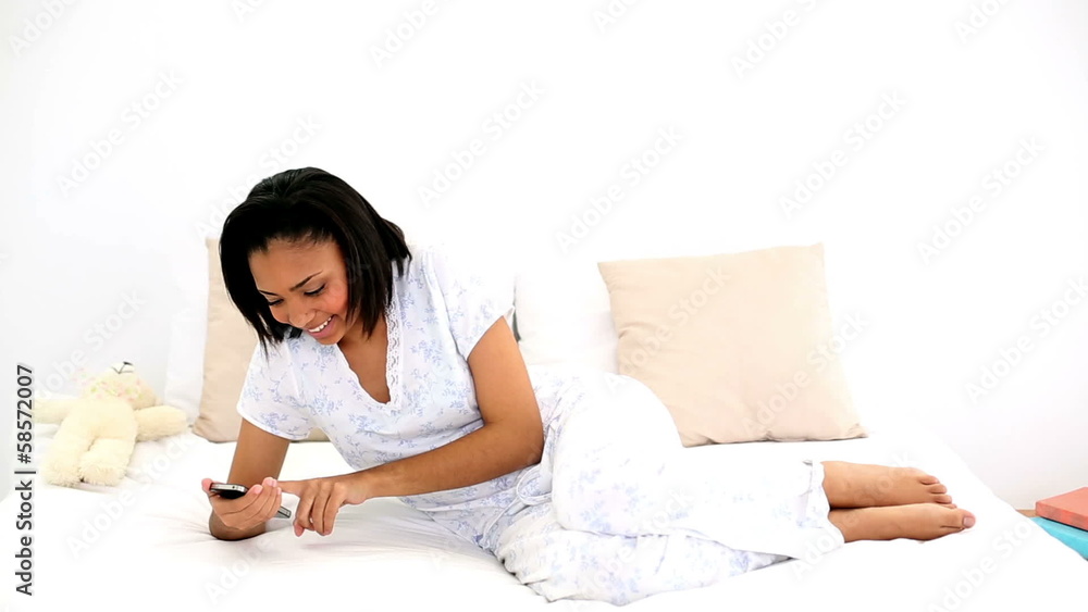 Dark haired woman messaging with her smartphone lying on her bed Dark haired woman messaging with her smartphone lying on her bed