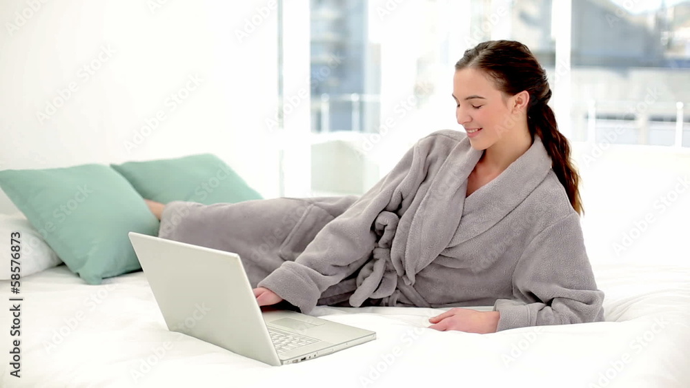 Peaceful brunette woman using her notebook wearing a bathrobe Peaceful brunette woman using her notebook wearing a bathrobe