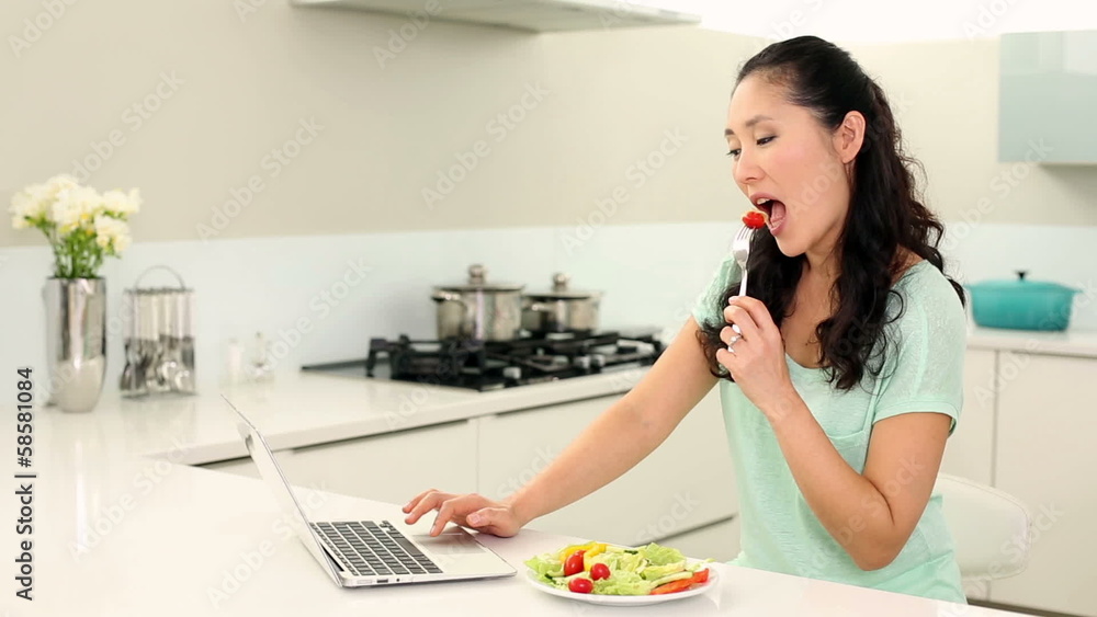 Pretty woman using laptop and eating salad Pretty woman using laptop and eating salad