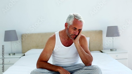 Hungover man sitting on the end of his bed and frowning
