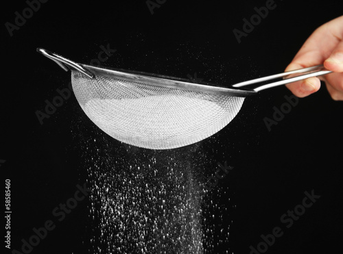 Sieve and powdered sugar on black background