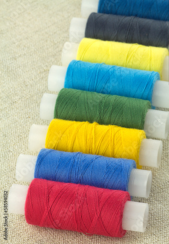Row of color threads spools on beige fabric close up