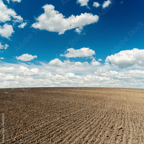 plowed field and deep blue sky with clouds over it