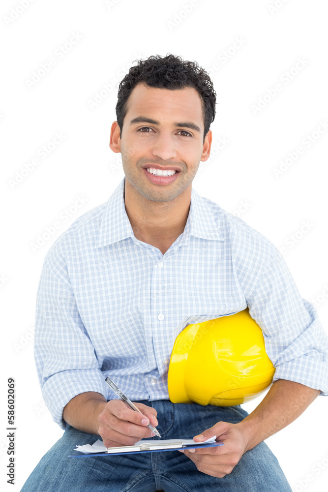 Smiling handyman with yellow hard hat writing in clipboard Smiling handyman with yellow hard hat writing in clipboard