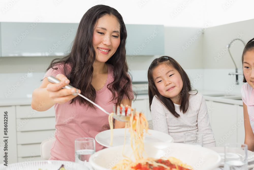 Girls watching happy woman serve spaghetti in kitchen Girls watching happy woman serve spaghetti in kitchen