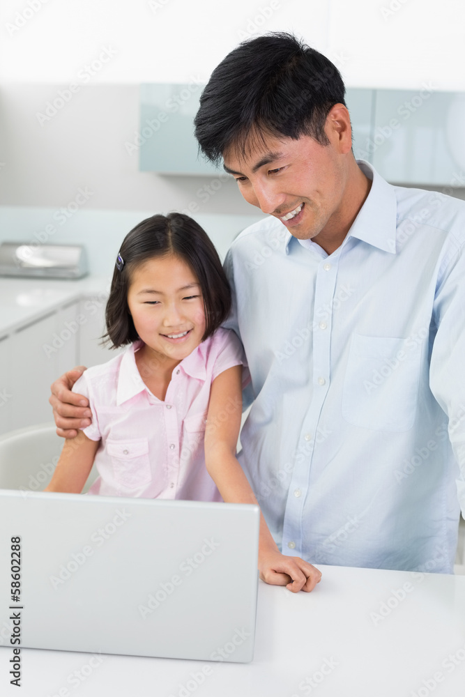 Smiling father with daughter using laptop in kitchen Smiling father with daughter using laptop in kitchen
