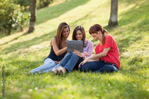 Three woman sitting on grass and looking at a digital tablet