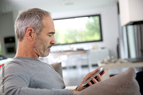 Senior man in couch reading message on smartphone