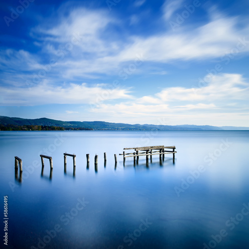 Fototapeta Naklejka Na Ścianę i Meble -  Wooden pier or jetty remains on a blue lake. Long Exposure.