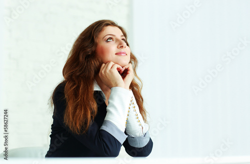 Happy young woman sitting at the table and looking up in office