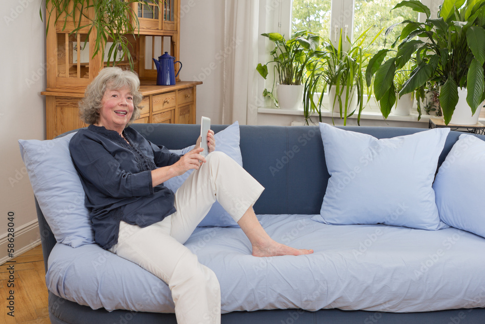 Obraz premium Smiliing elderly woman with tablet pc on couch