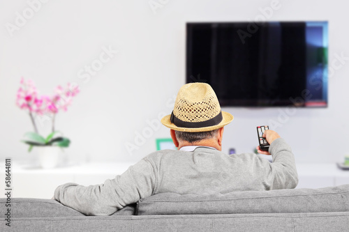 Man with hat sitting on a sofa and changing channels at home © Ljupco Smokovski