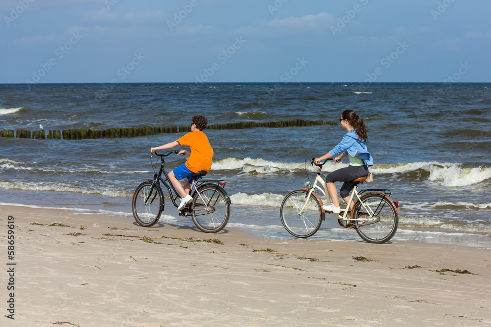Fototapeta premium Teenage girl and boy biking on beach