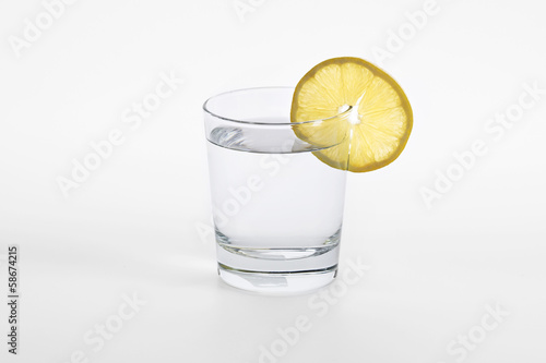 Glass with water and piece of a lemon on a white background