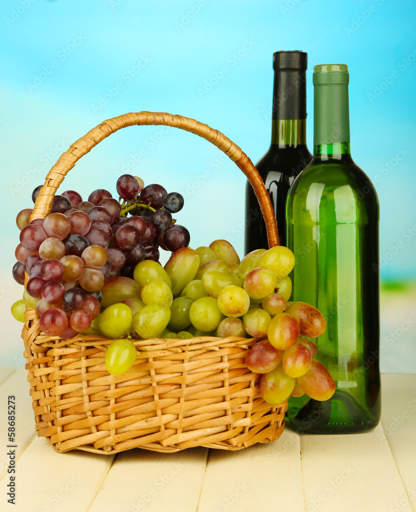 Ripe grapes in wicker basket, wine bottles, on bright