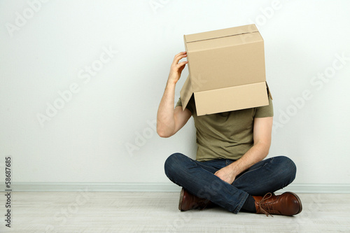 Man with cardboard box on his head sitting on floor near wall