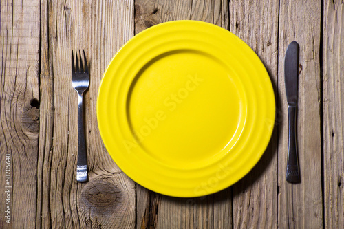 Cutlery and yellow plate on  wooden table