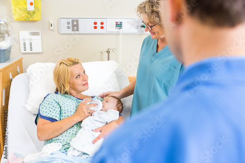 Nurse Looking At Woman Feeding Milk To Babygirl In Hospital