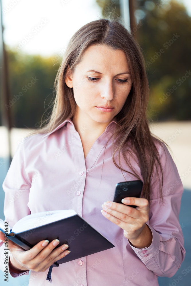 Young businesswoman with cellphone and organizer while standing Young businesswoman with cellphone and organizer while standing
