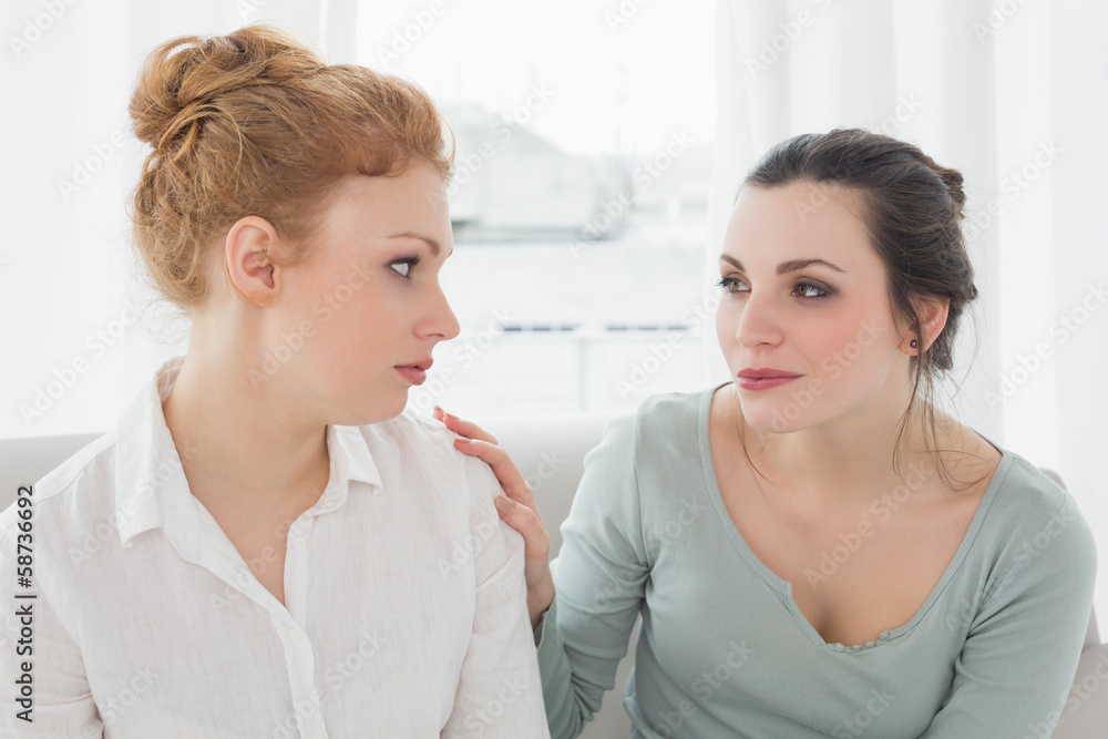 Young woman consoling female friend on sofa Young woman consoling female friend on sofa