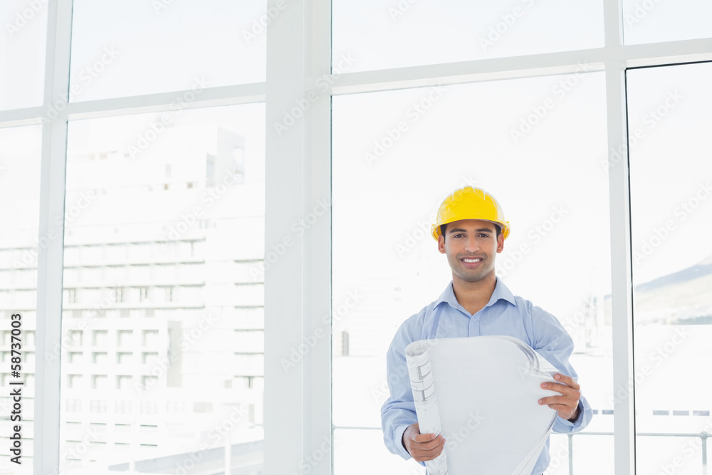Smiling architect in yellow hard hat with blueprint in office Smiling architect in yellow hard hat with blueprint in office