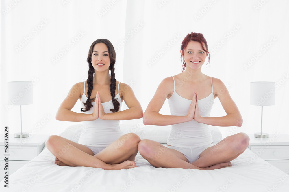 Two young women sitting with joined hands on bed Two young women sitting with joined hands on bed