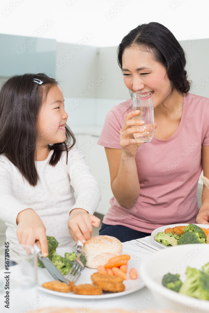 Mother watching little girl eat food in kitchen Mother watching little girl eat food in kitchen