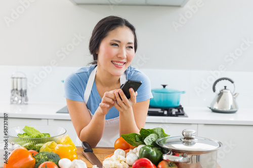 Smiling woman text messaging in front of vegetables in kitchen