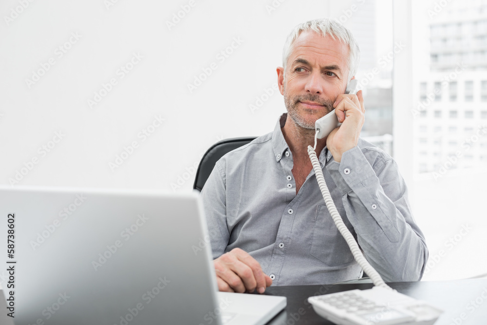 Businessman on call in front of laptop at office desk Businessman on call in front of laptop at office desk