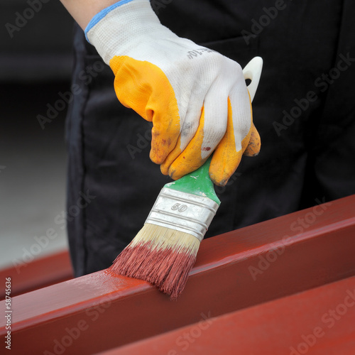 Worker painting steel tube with paint brush focus on hand