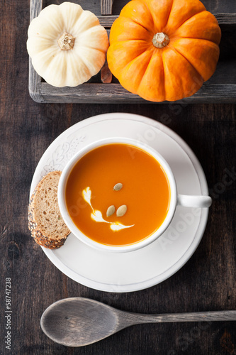 Pumpkin soup with pumpkin seeds in a white cup and raw pumpkins