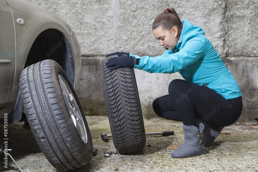 Young  woman driver replacing summer tyres with winter tyres