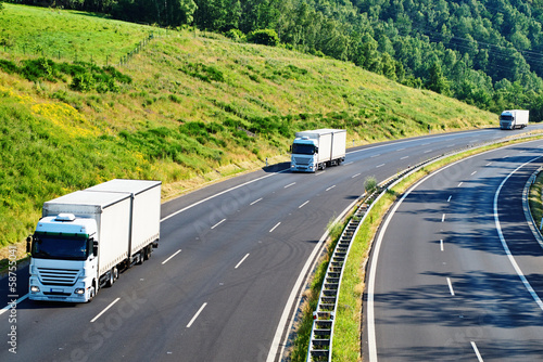 Highway with three oncoming white truck in a wooded landscape