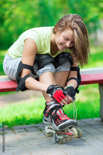 Girl going rollerblading sitting in bench putting on inline skat