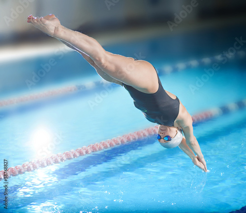 Female swimmer, that jumping into indoor swimming pool.