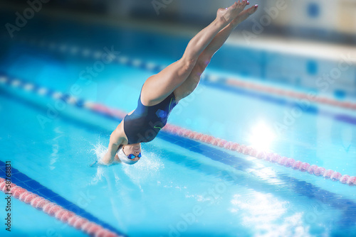Female swimmer, that jumping into indoor swimming pool.