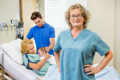 Mature Nurse Standing With Couple And Newborn Baby In Background