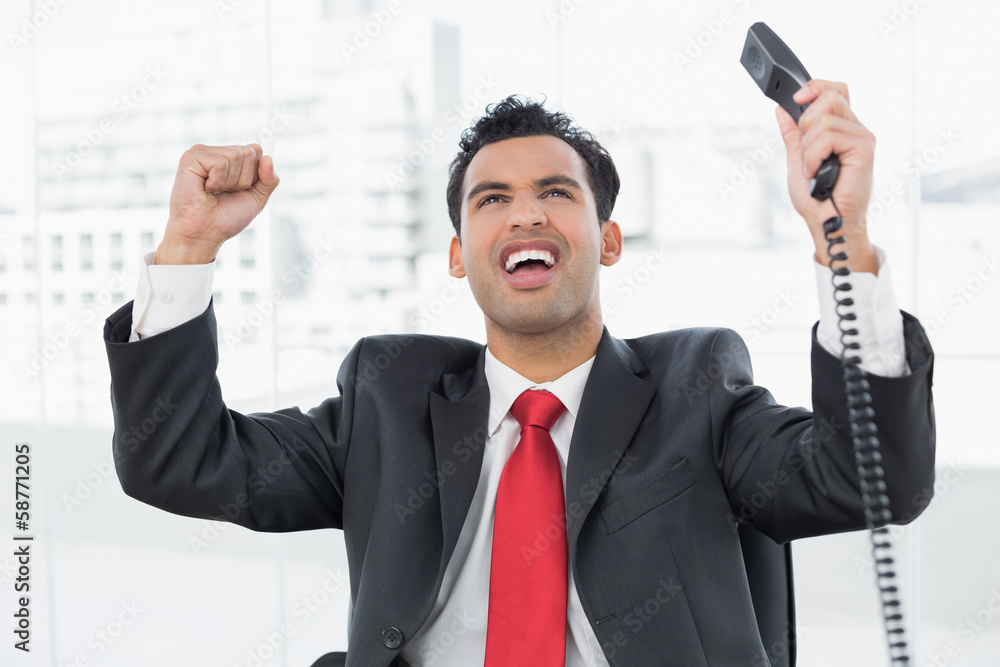 Naklejka premium Businessman cheering with telephone receiver at office