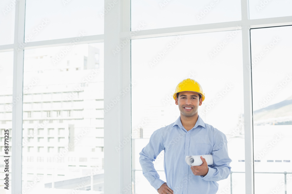 Young architect in yellow hard hat with blueprint in office