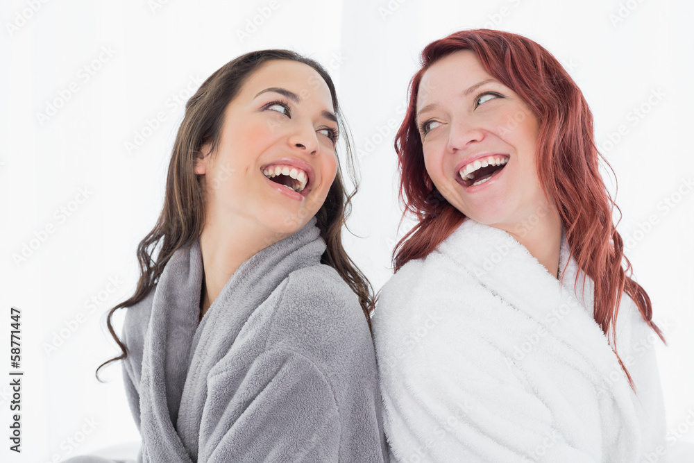 Happy female friends in bathrobes standing back to back Happy female friends in bathrobes standing back to back