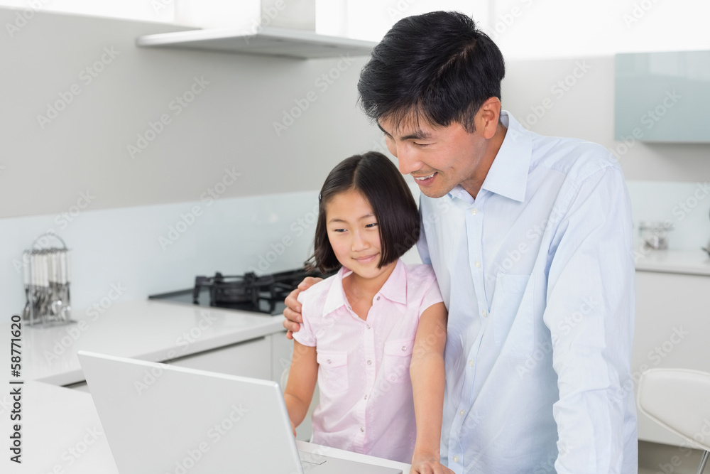 Smiling father and daughter using laptop in kitchen Smiling father and daughter using laptop in kitchen