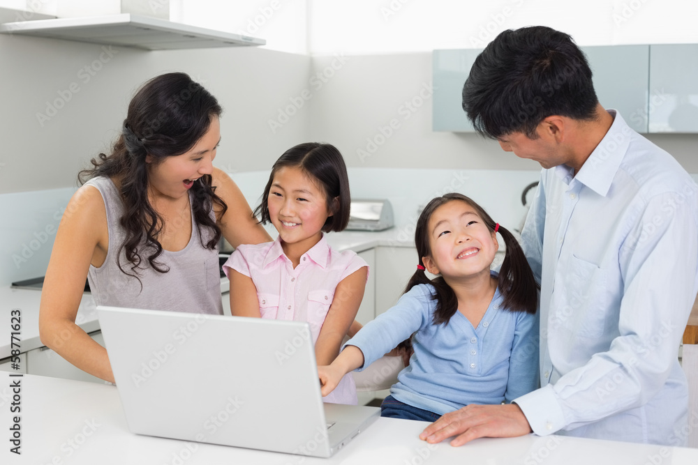 Happy family of four using laptop in kitchen