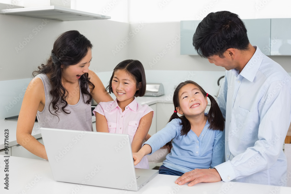 Happy family of four using laptop in kitchen Happy family of four using laptop in kitchen