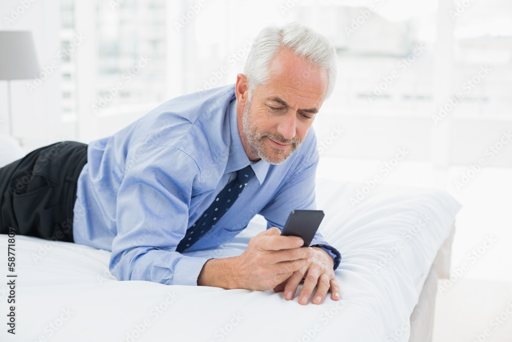 Smiling relaxed businessman text messaging in bed Smiling relaxed businessman text messaging in bed