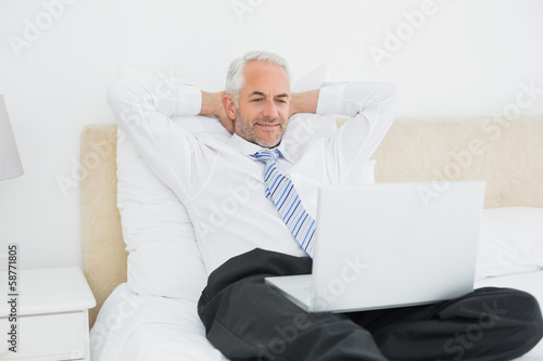 Relaxed businessman looking at laptop in bed © lightwavemedia