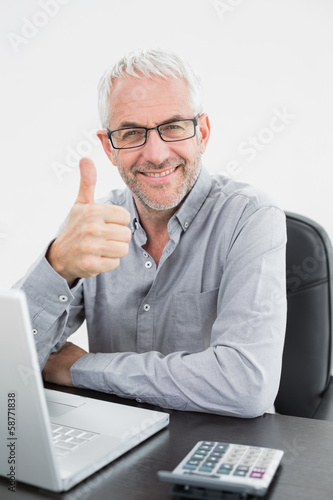 Smiling businessman with laptop gesturing thumbs up