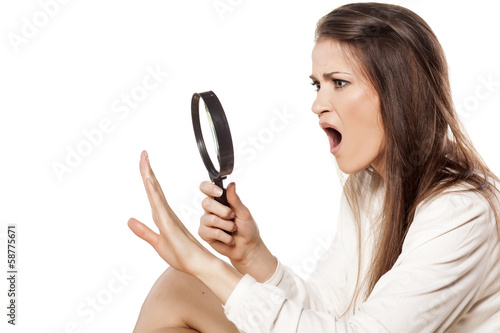 shocked young woman looking through a magnifying glass her nails