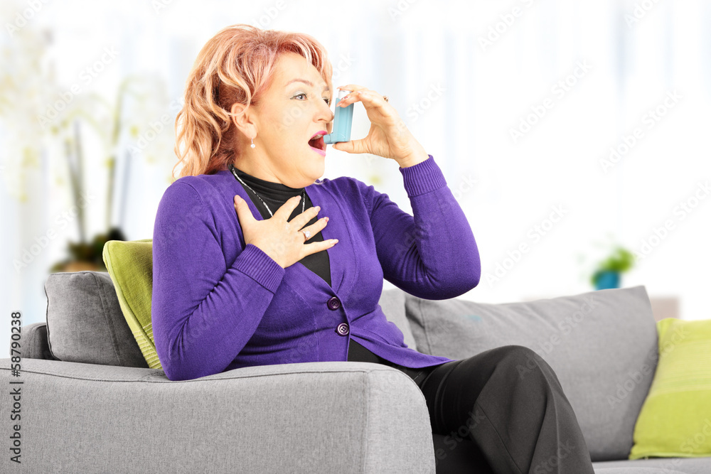 Mature woman on a sofa taking asthma treatment with inhaler Mature woman on a sofa taking asthma treatment with inhaler